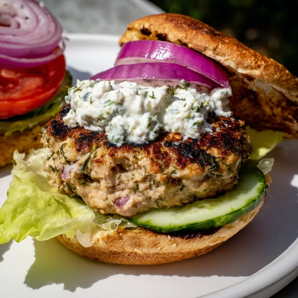 Golden grilled Greek chicken burgers topped with creamy tzatziki sauce and fresh vegetables on toasted buns