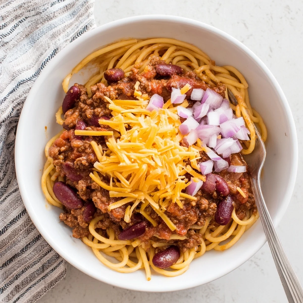 Steaming plate of Cincinnati Chili over spaghetti topped with melted cheddar cheese and diced onions