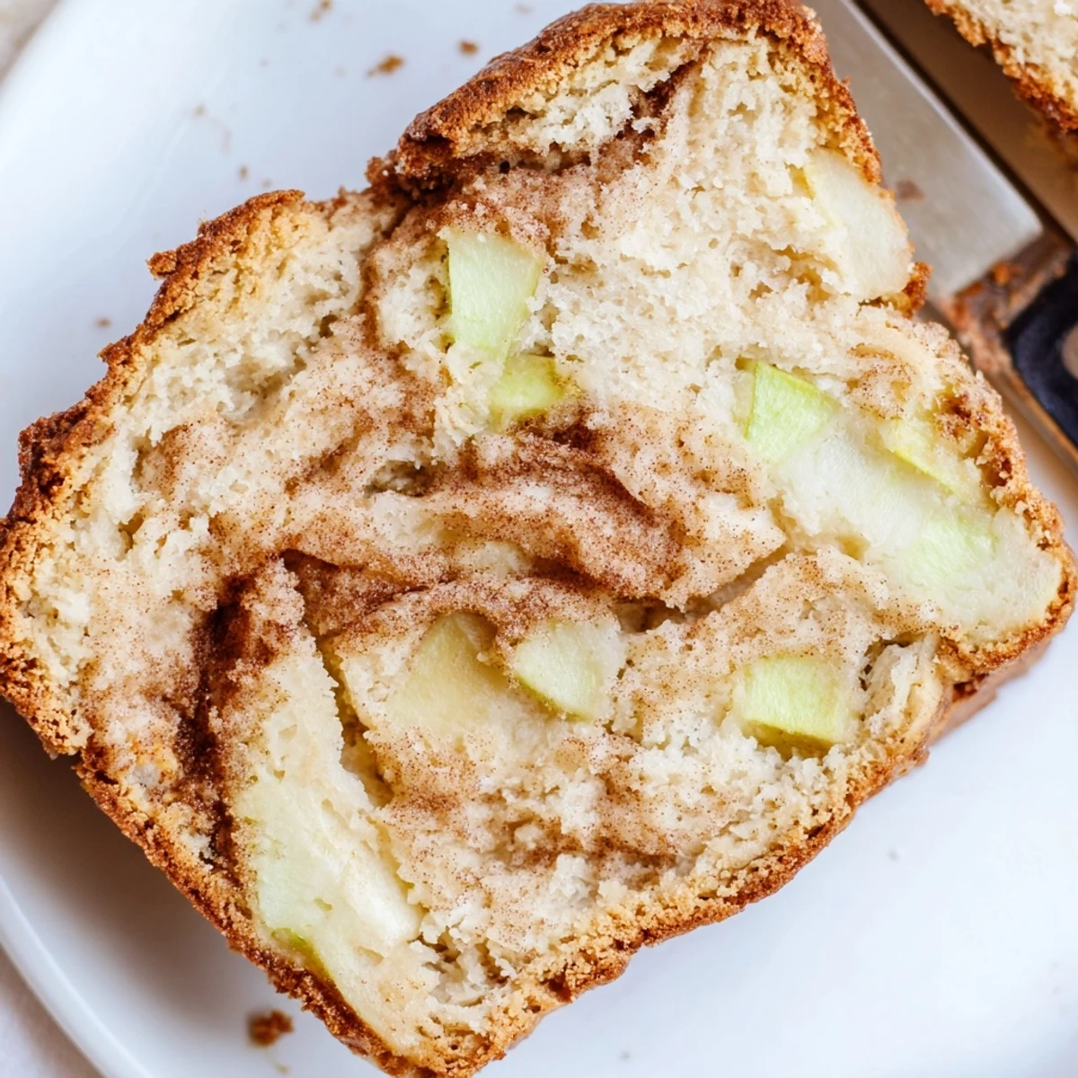 Golden brown cinnamon apple bread loaf with visible apple chunks and sugary cinnamon swirl topping