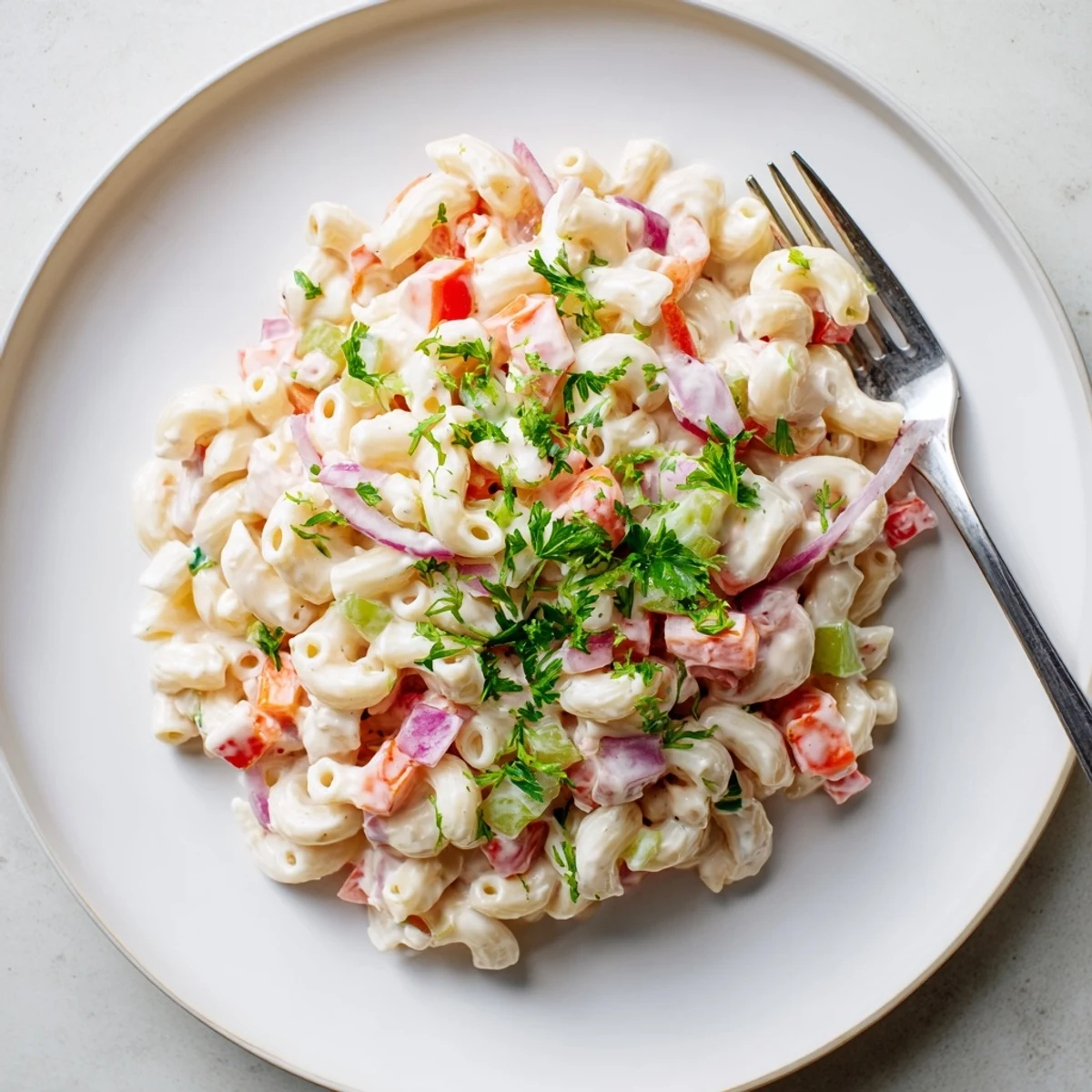 Tangy And Creamy Macaroni Salad chilled in white bowl showcasing vibrant red peppers and green celery
