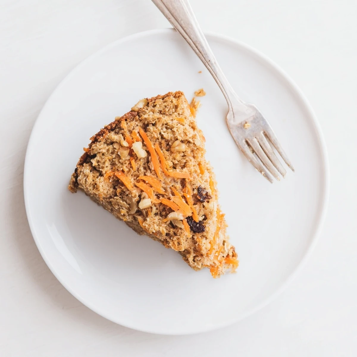 Moist flourless oatmeal carrot cake slice topped with chopped walnuts on a white plate