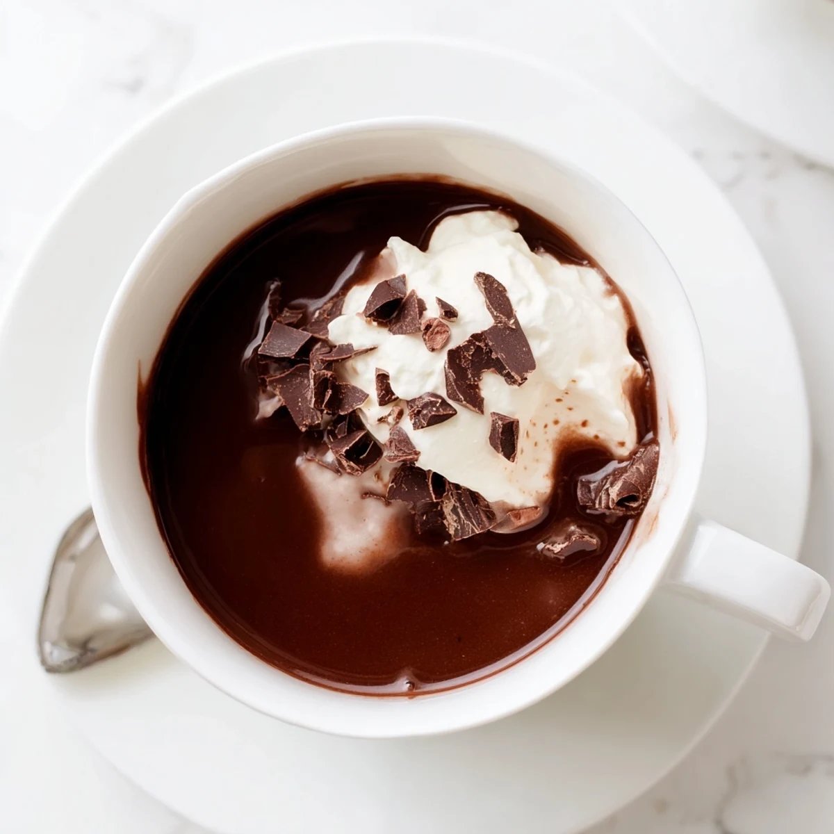 Creamy keto hot chocolate in a white mug topped with sugar-free whipped cream and dark chocolate shavings
