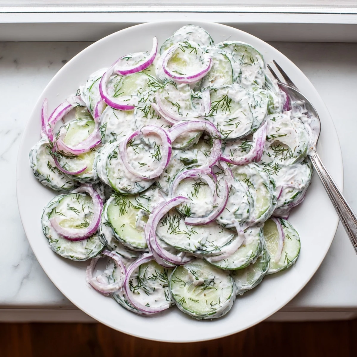 Crisp cucumber dill salad topped with fresh dill in a white serving bowl