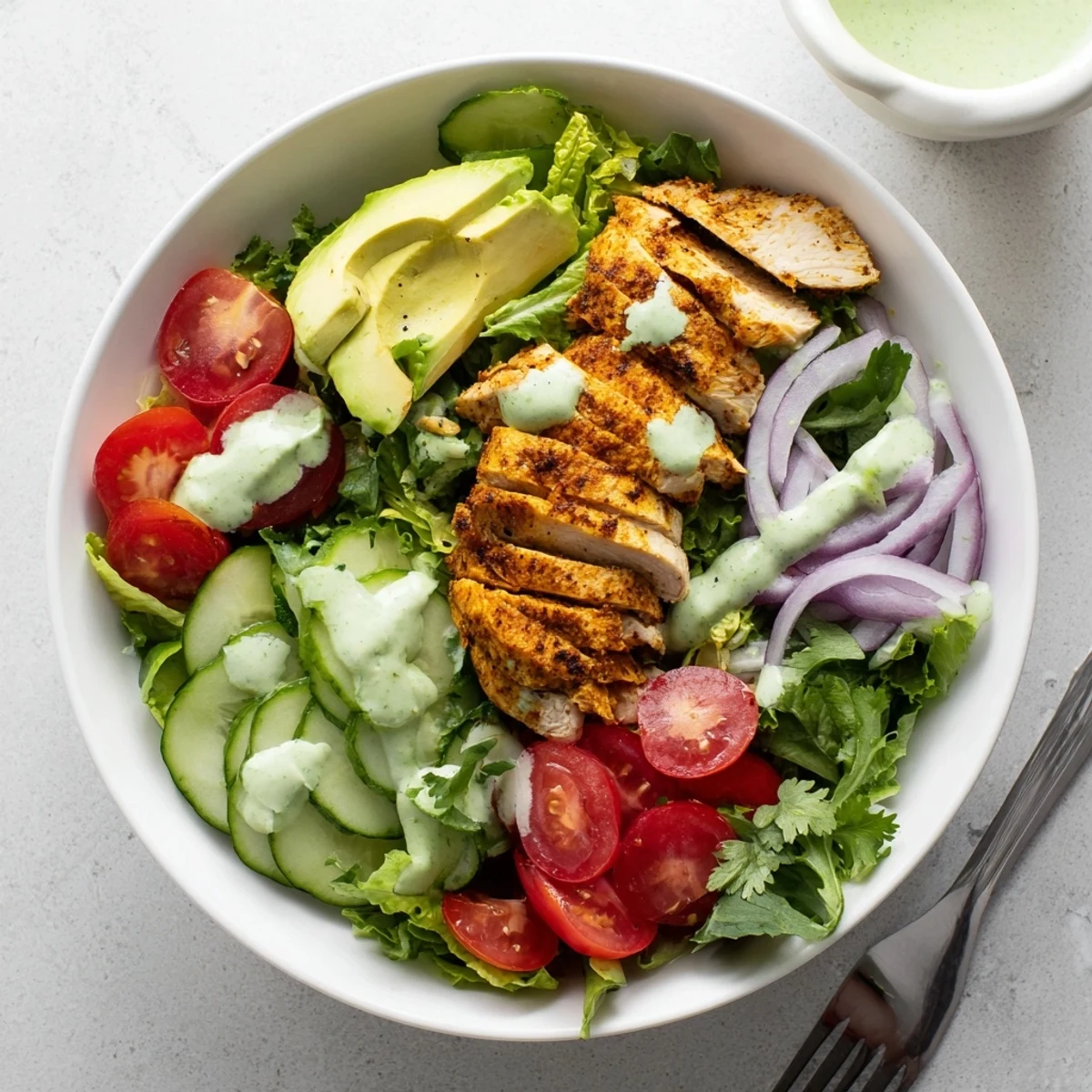 Colorful bowl of creamy avocado grilled chicken salad with fresh vegetables and tangy green dressing drizzled on top