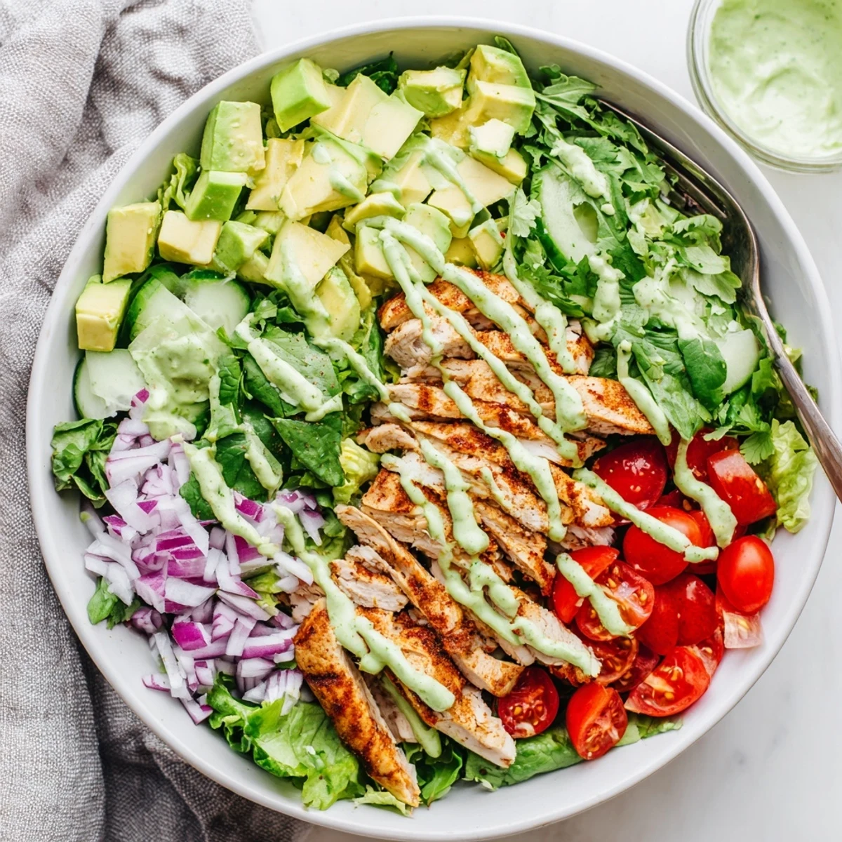 Sliced grilled chicken breasts rest over vibrant mixed greens, cherry tomatoes, cucumber and creamy avocado chunks in a wholesome meal prep bowl