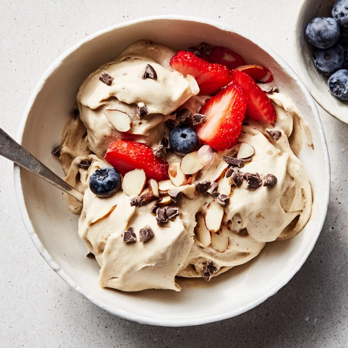 Soft-serve style banana nice cream scooped into a colorful bowl with sliced banana wheels and crushed almond pieces