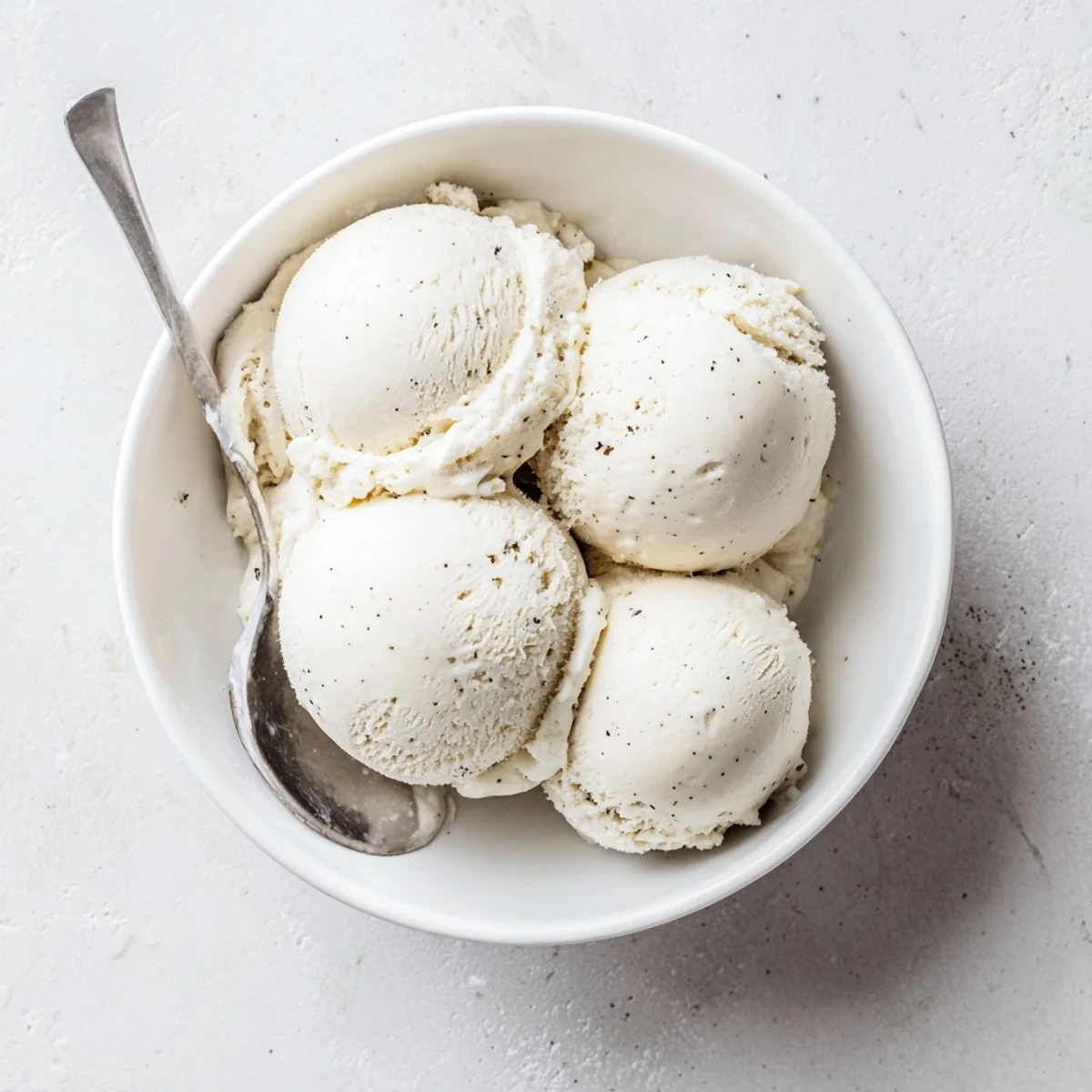 Creamy homemade vanilla ice cream scooped into a chilled glass bowl with a silver spoon