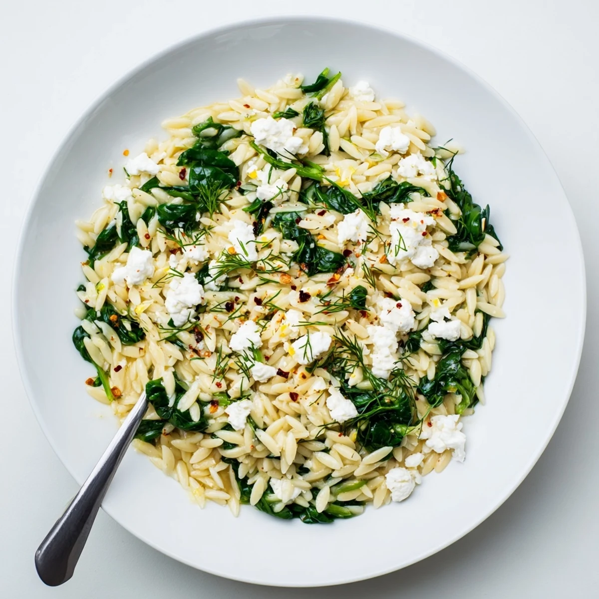 Golden one pan lemon orzo with wilted spinach and crumbled feta cheese in a skillet