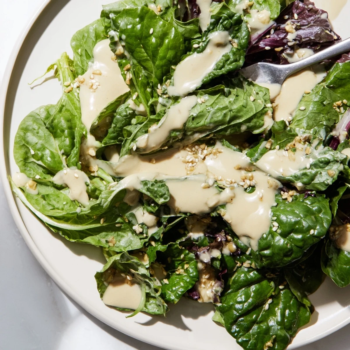 Creamy sesame dressing drizzled over fresh green salad in white bowl