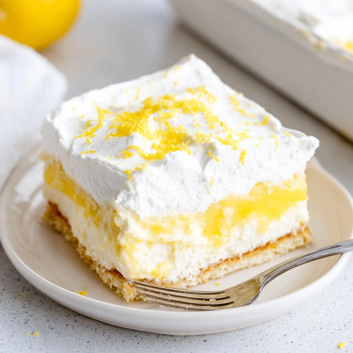 Square serving of Lemon Lush Cake topped with billowy whipped cream and fresh lemon zest