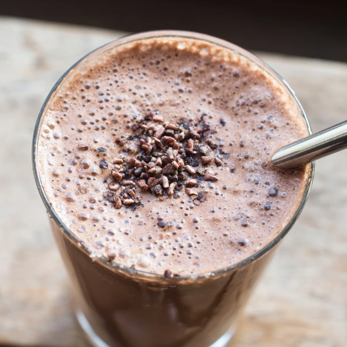 Glass of thick raw chocolate banana shake topped with cacao nibs and coconut flakes