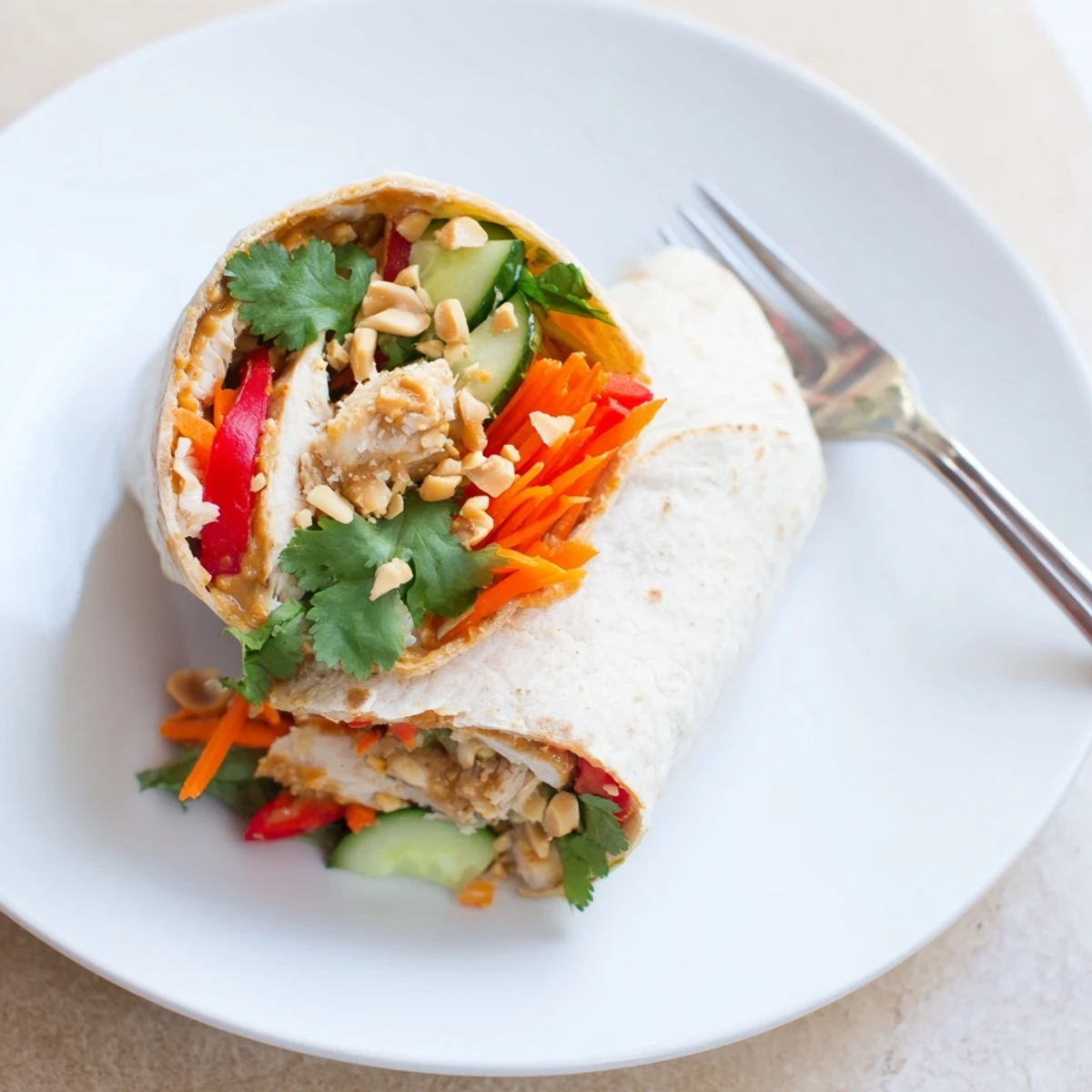Sliced grilled chicken layered with colorful peppers, carrots, and cucumbers inside Thai peanut chicken wraps