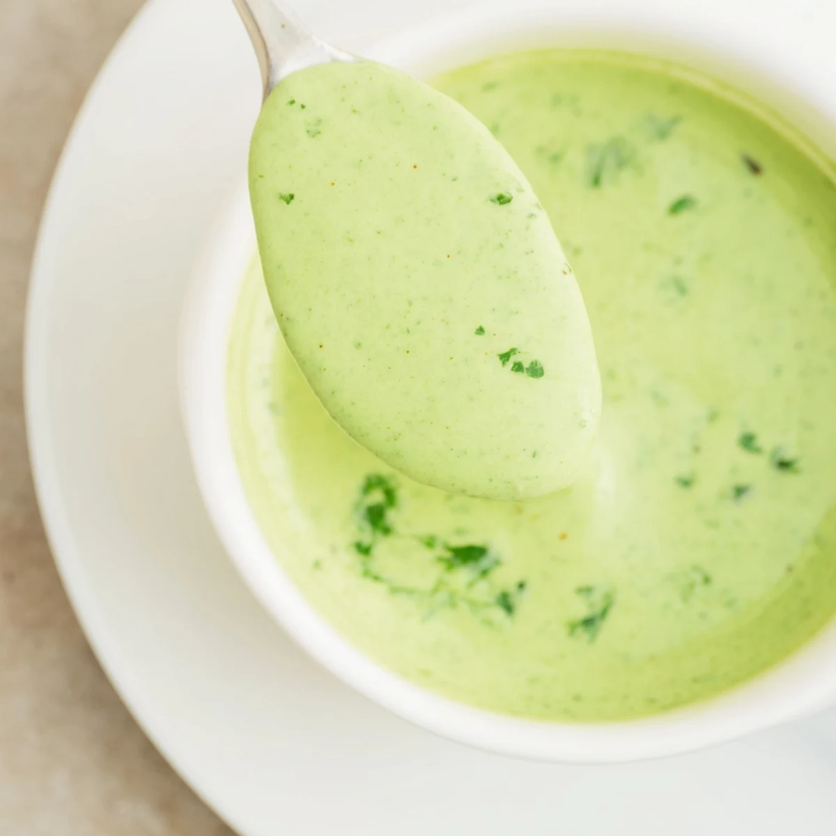 Vibrant green cilantro lime sauce in a small white bowl garnished with extra herbs