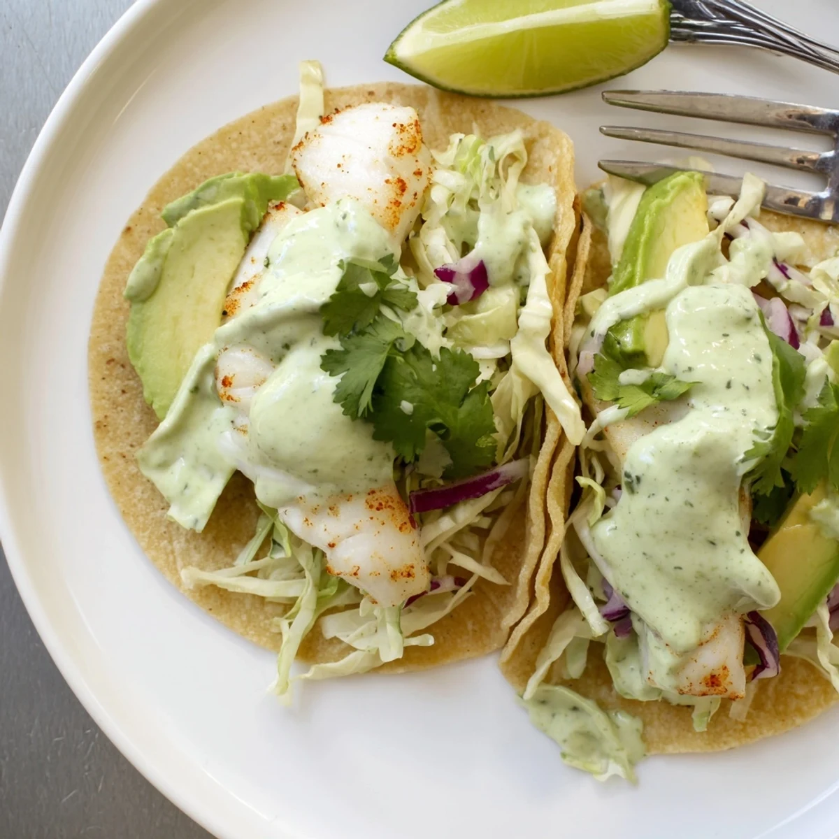 Flaky Baked Cod Fish Tacos with Creamy Cilantro Lime Sauce topped with crisp slaw