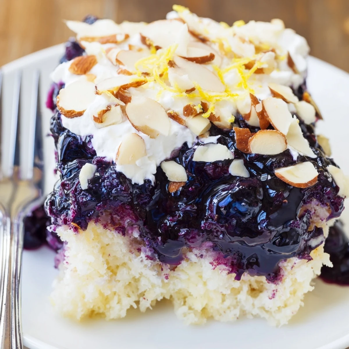 Chilled slice on floral plate highlights Lemon Blueberry Poke Cake With Almond Topping