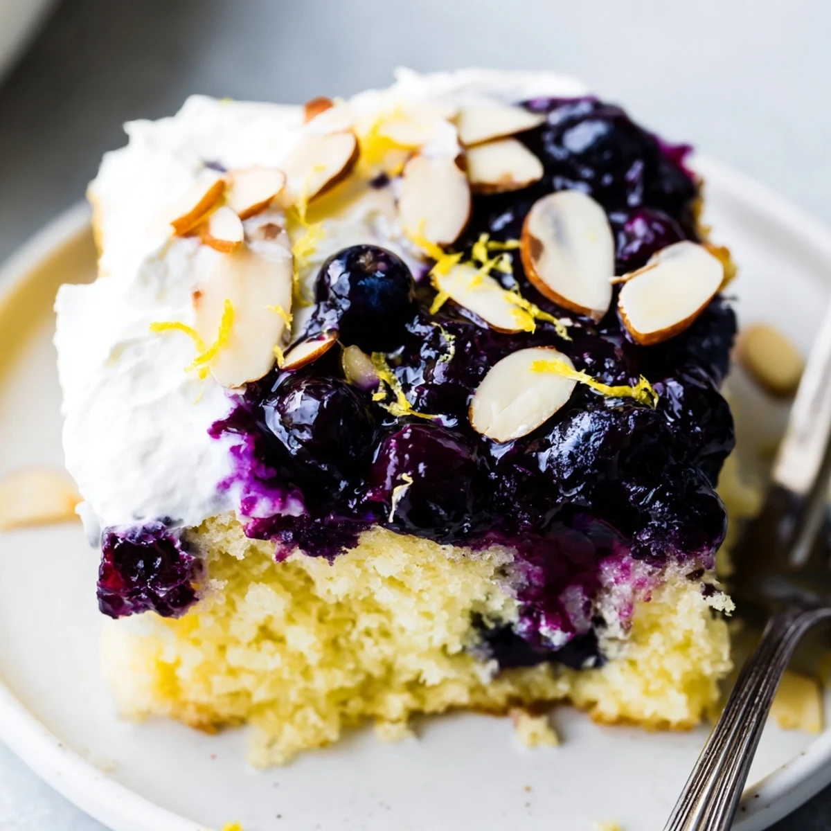 Whipped almond cream crowns bright lemon cake — Lemon Blueberry Poke Cake With Almond Topping
