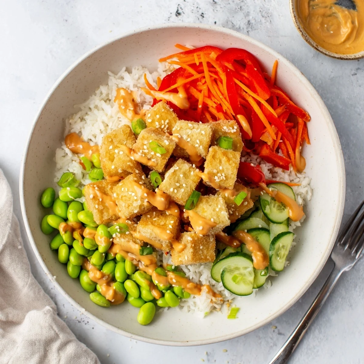 Creamy peanut sauce cascading over a vibrant tofu rice bowl with colorful vegetables