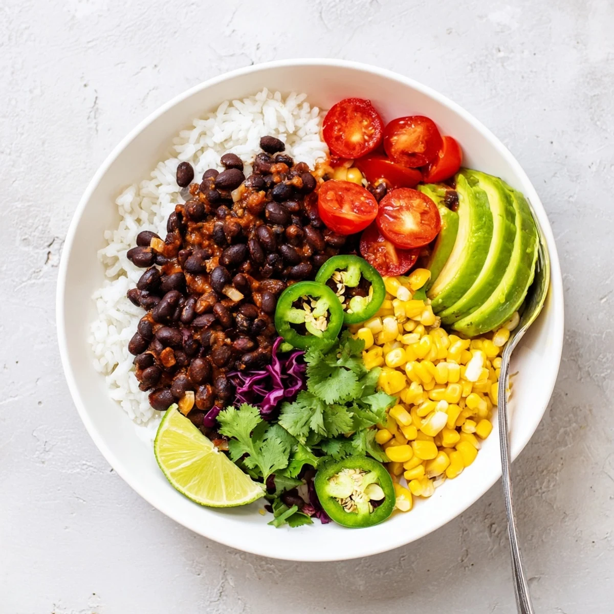 Hearty black bean and rice bowl topped with fresh avocado, tomatoes, and lime wedges