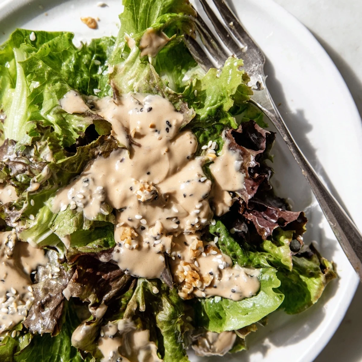 Creamy sesame dressing drizzled over fresh green salad in white bowl
