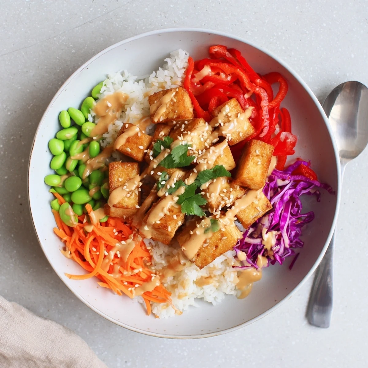 Crispy golden tofu rice bowl with peanut sauce drizzled over colorful fresh vegetables