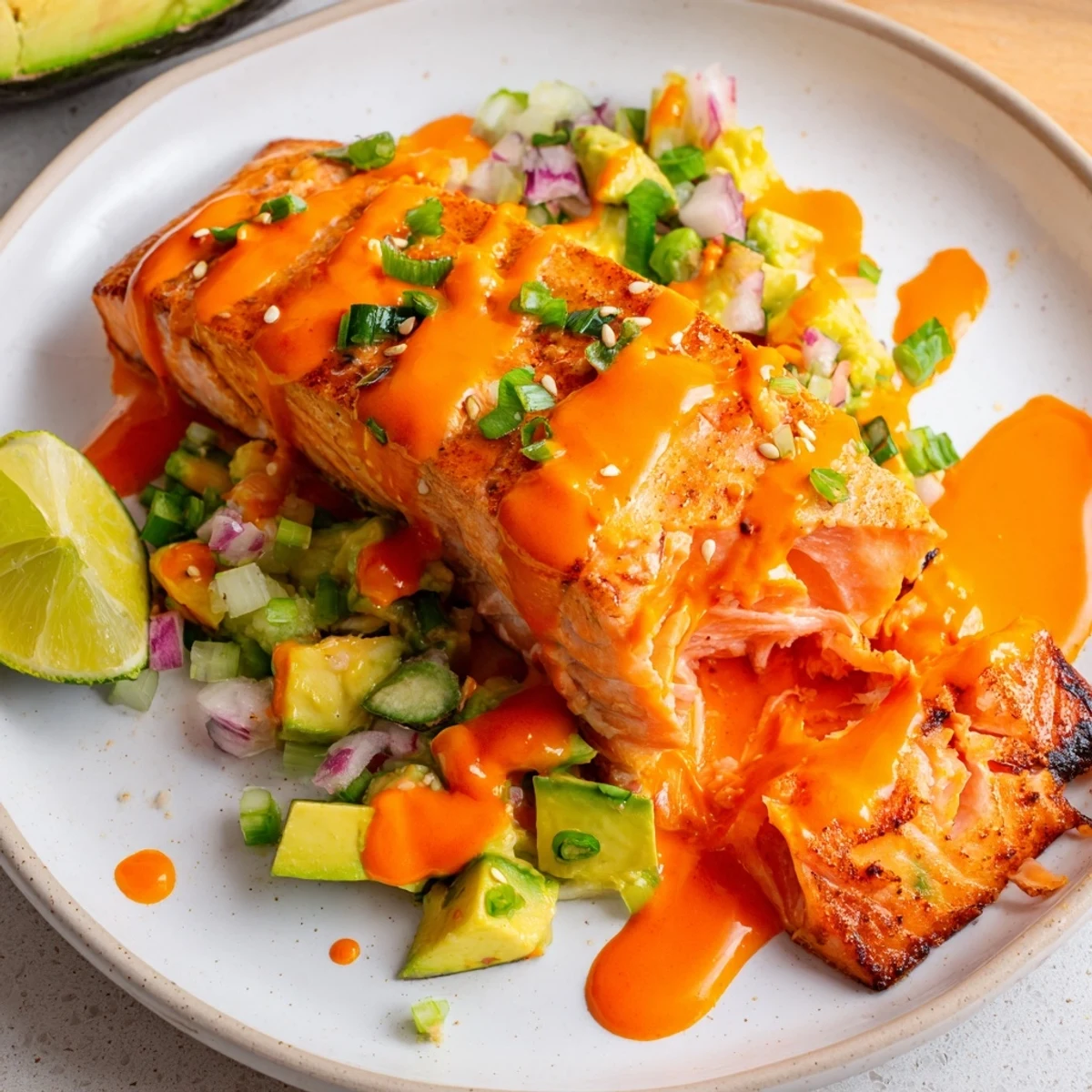 Golden pan-seared Bang Bang Salmon topped with creamy sriracha sauce served over vibrant avocado cucumber salsa