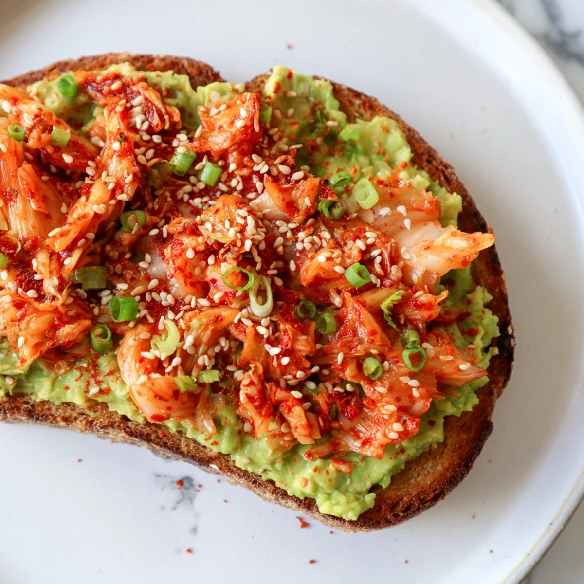 Creamy avocado and spicy kimchi piled on golden sourdough toast with sesame seeds