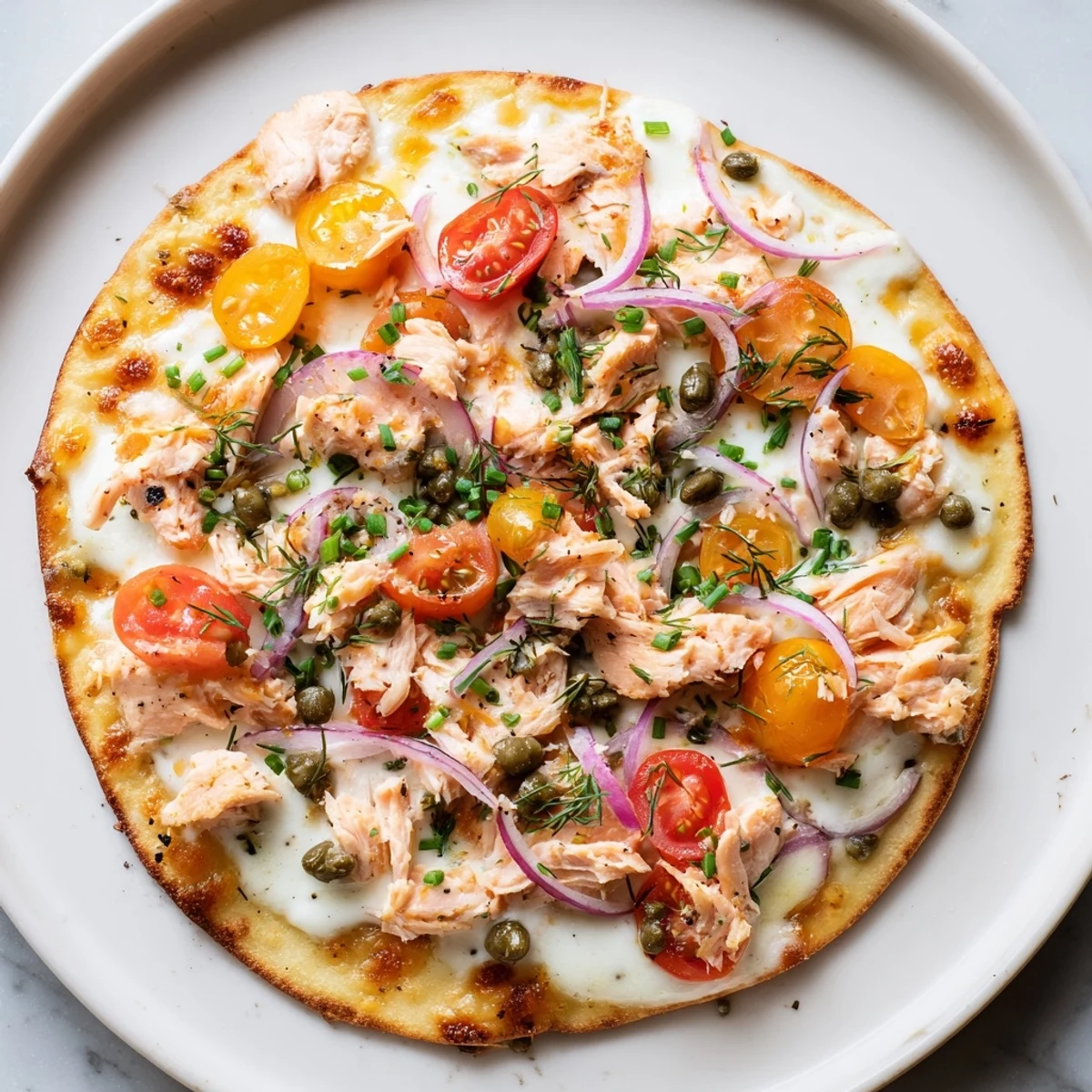 Golden baked salmon tortilla pizza topped with capers, red onion, and bubbling cheese