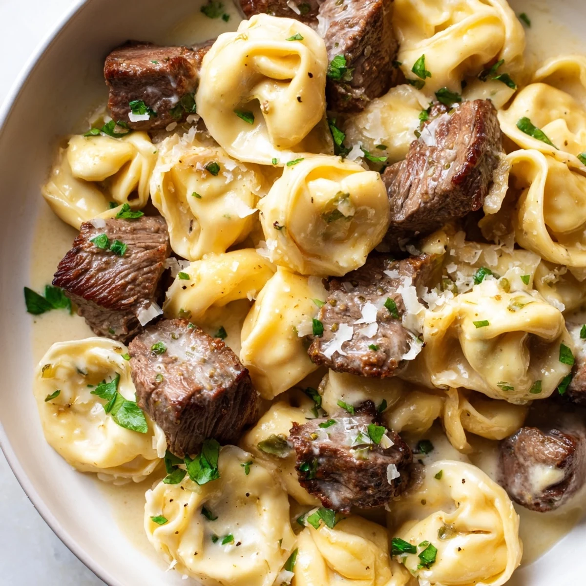 Sizzling steak bites served alongside cheesy garlic steak tortellini in a creamy white skillet sauce