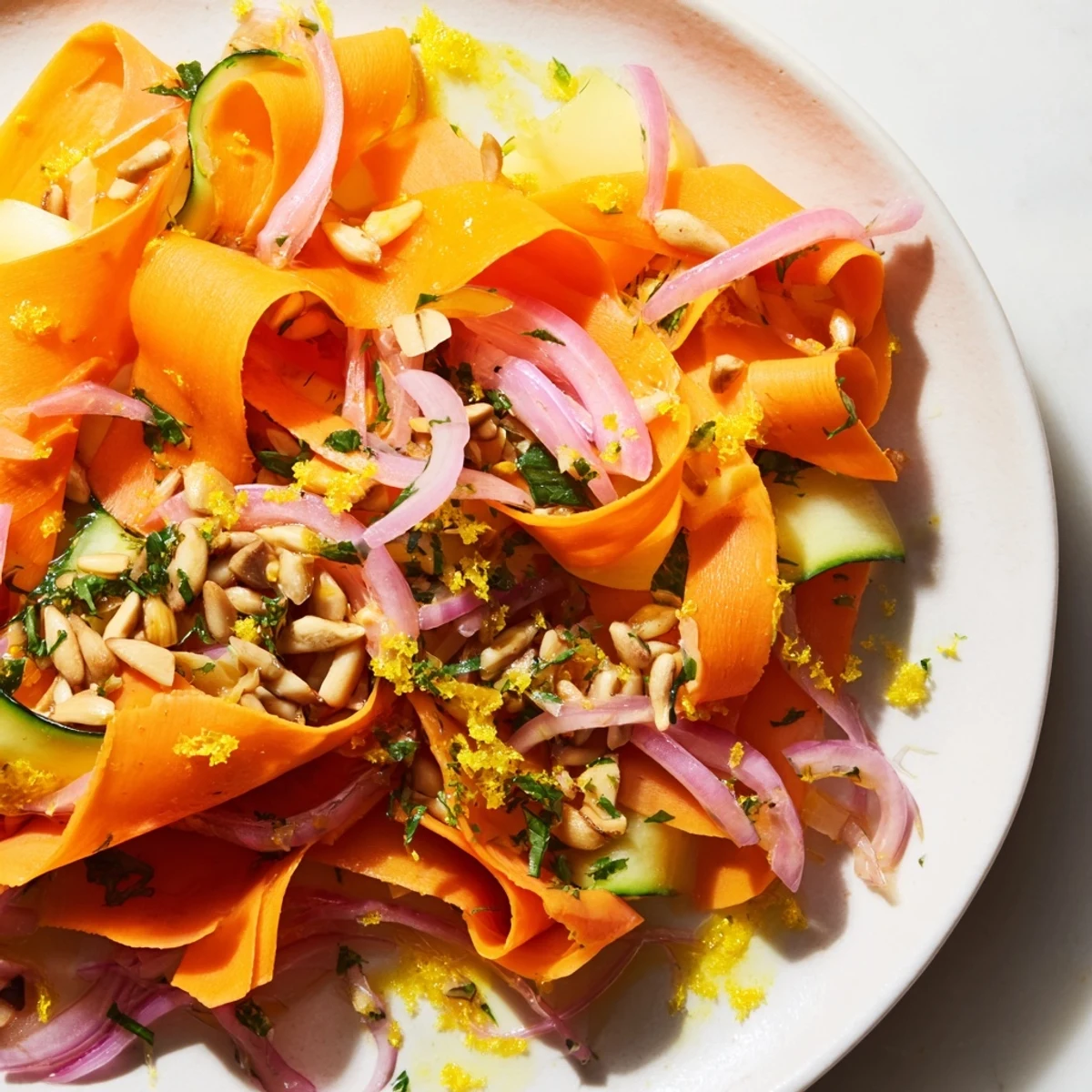 Vibrant carrot ribbon salad topped with crunchy sunflower seeds and red onion.