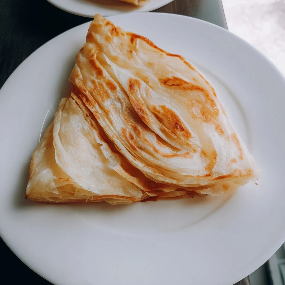 Golden flaky Roti Canai flatbread served with a side of rich curry.  