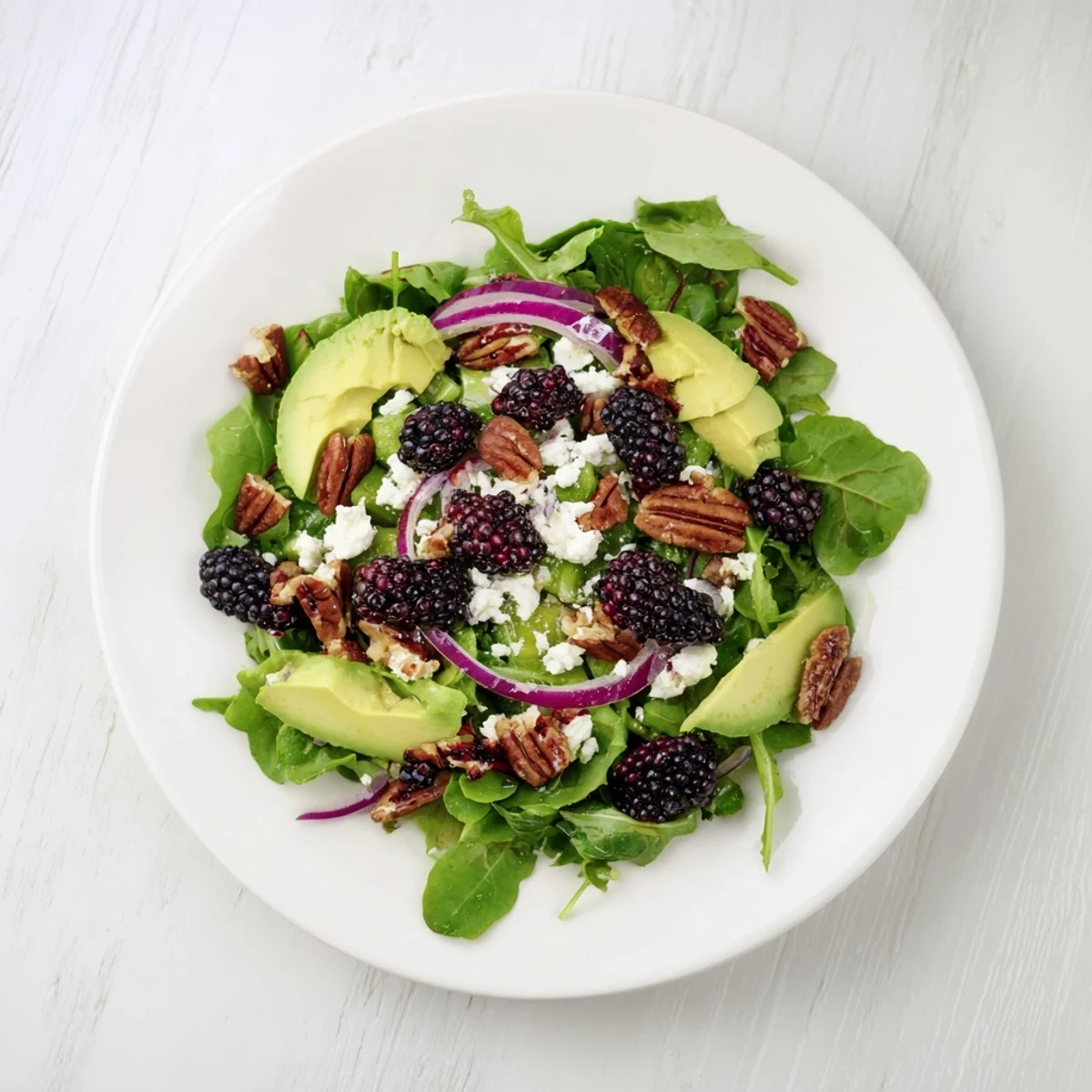 Colorful bowl of blackberry avocado salad topped with feta and crunchy toasted pecans.