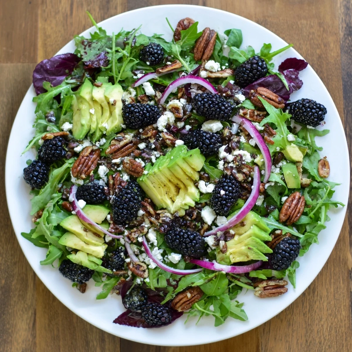 Vibrant blackberry avocado salad featuring arugula, red onion, and zesty lime dressing drizzled over.