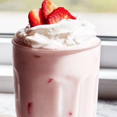 Cold strawberry milkshake in a tall glass garnished with fluffy whipped topping