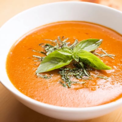 Bowl of creamy roasted tomato basil soup served with crusty bread slices.