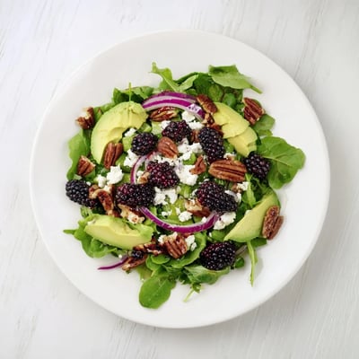 Colorful bowl of blackberry avocado salad topped with feta and crunchy toasted pecans.